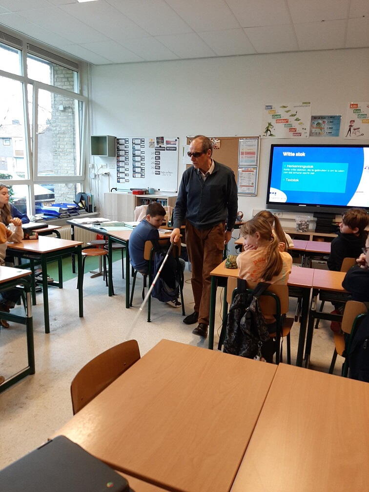 Man met taststok in klaslokaal tussen leerlingen